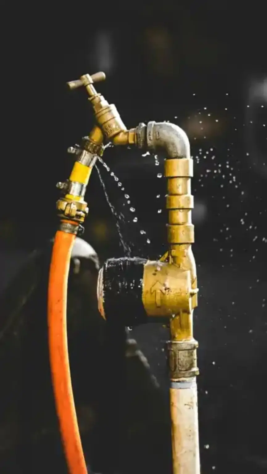 Orange garden hose connected to an outside tap with visible spraying leaks
