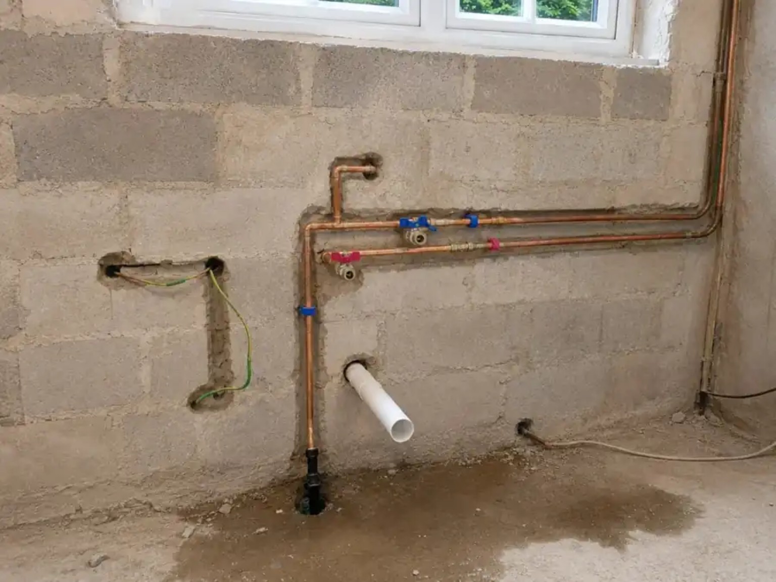 First-fix copper water pipework and waste connections on an unfinished block wall
