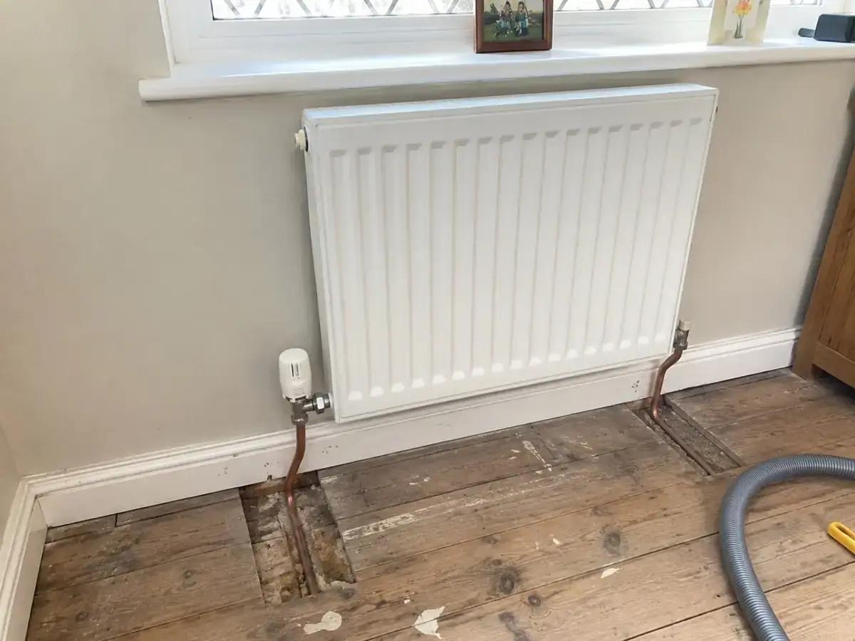 Radiator repositioned with exposed floorboards showing altered pipe routes