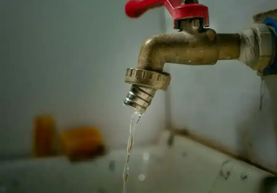 Outside garden tap with a red handle and a visible drip